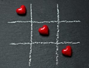Tic tac toe board on black surface with red heart shapes symbolizing love and connection.